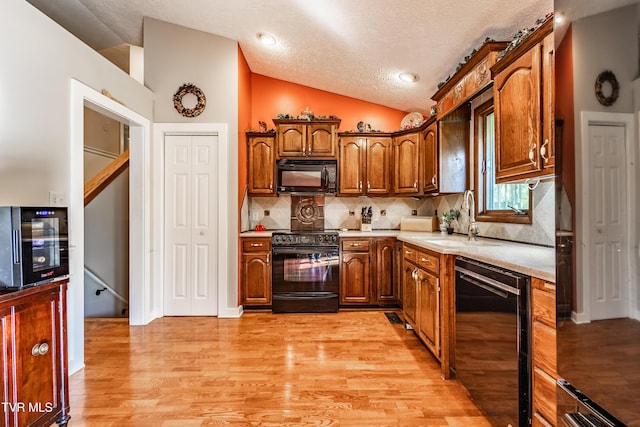 kitchen featuring black appliances, a sink, vaulted ceiling, light wood-style flooring, and beverage cooler