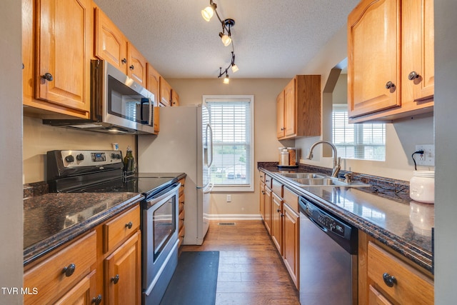 kitchen with dark wood finished floors, appliances with stainless steel finishes, a sink, baseboards, and a textured ceiling