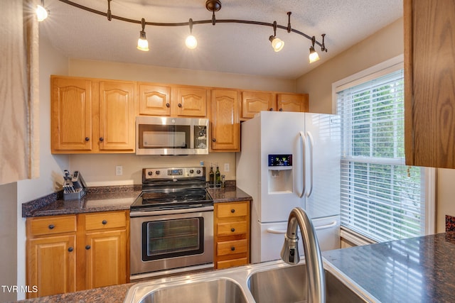 kitchen with a textured ceiling, dark countertops, stainless steel appliances, and a sink