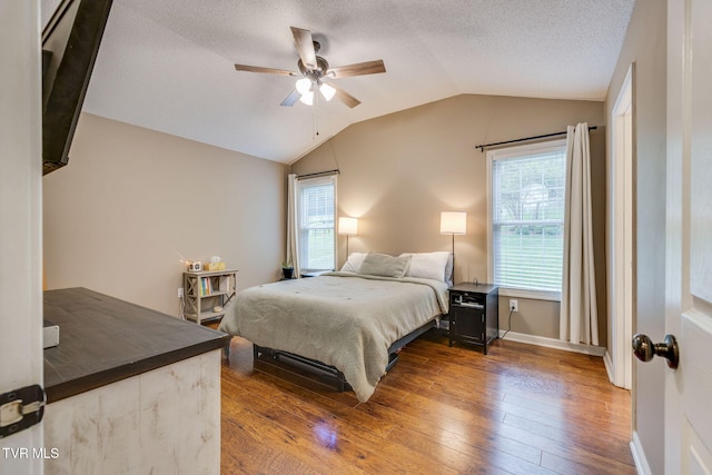 bedroom featuring lofted ceiling, a textured ceiling, hardwood / wood-style flooring, baseboards, and a ceiling fan