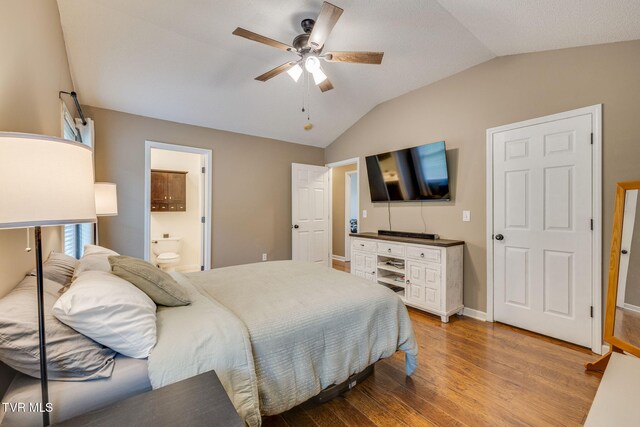 bedroom with light wood-type flooring, a ceiling fan, baseboards, lofted ceiling, and ensuite bathroom