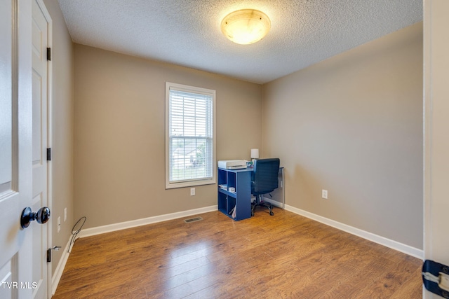 unfurnished office with a textured ceiling, visible vents, wood finished floors, and baseboards