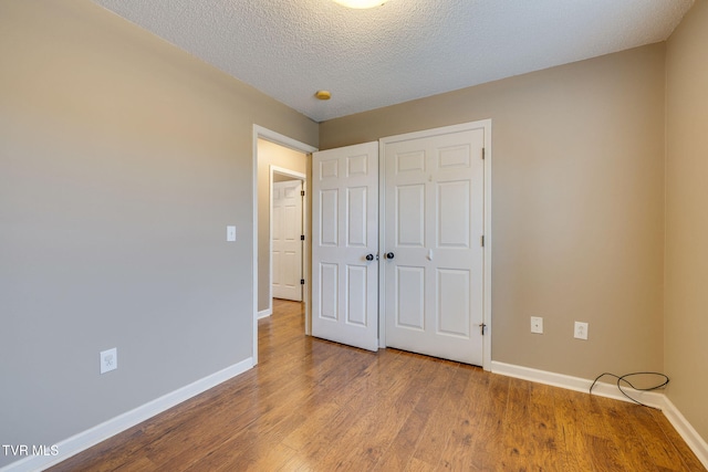 unfurnished bedroom with baseboards, wood finished floors, a textured ceiling, and a closet