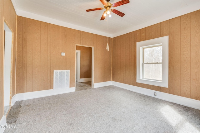 unfurnished room featuring wooden walls, visible vents, ceiling fan, and carpet flooring
