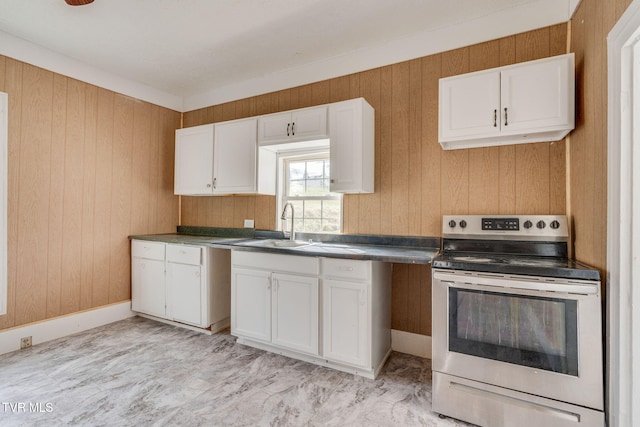 kitchen featuring baseboards, wooden walls, white cabinets, stainless steel electric stove, and a sink