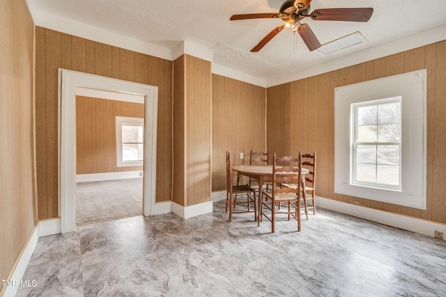 dining area featuring a textured ceiling, wood walls, and a ceiling fan