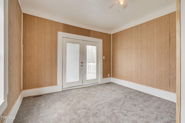 spare room with a ceiling fan, visible vents, carpet flooring, french doors, and wooden walls