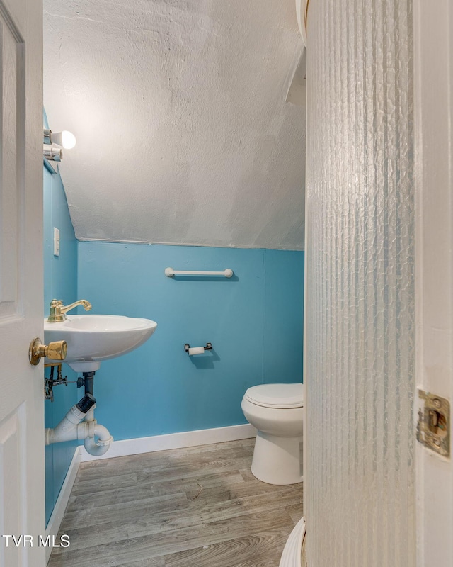 bathroom with a textured ceiling, vaulted ceiling, toilet, and wood finished floors