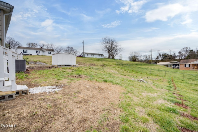 view of yard with central air condition unit, a rural view, a storage shed, an outdoor structure, and fence