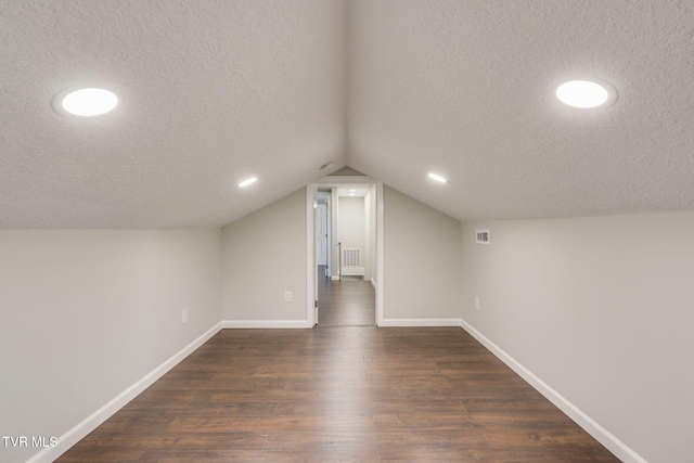 additional living space featuring a textured ceiling, dark wood-type flooring, baseboards, vaulted ceiling, and recessed lighting
