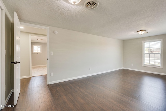 empty room with dark wood-style flooring, a textured ceiling, and baseboards
