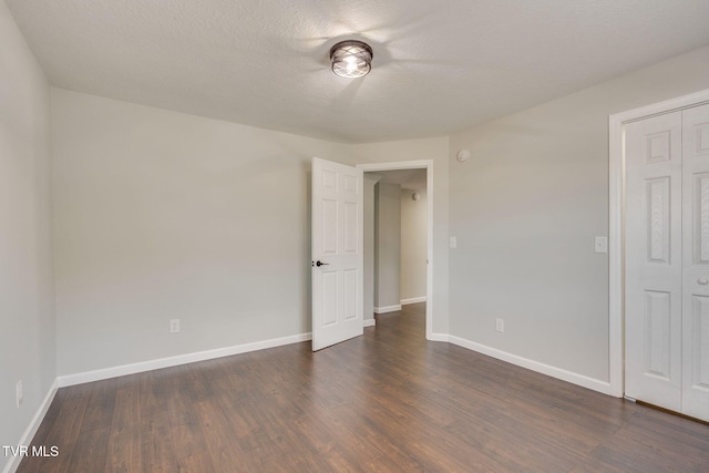 empty room with dark wood-type flooring, baseboards, and a textured ceiling
