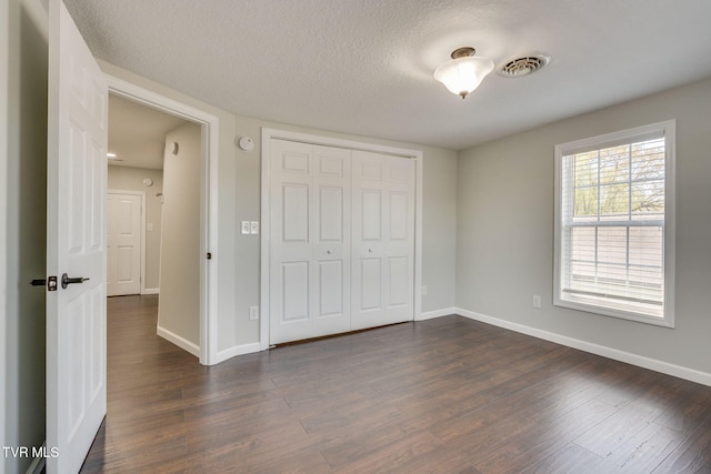 unfurnished bedroom with dark wood finished floors, baseboards, a closet, and a textured ceiling