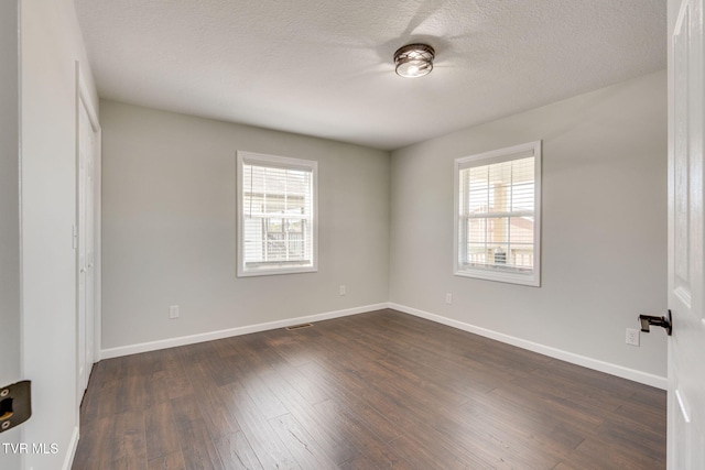unfurnished bedroom featuring multiple windows, dark wood finished floors, baseboards, and a textured ceiling