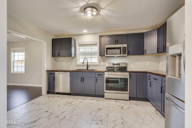 kitchen featuring stainless steel appliances, a sink, butcher block counters, light marble finish flooring, and a textured ceiling