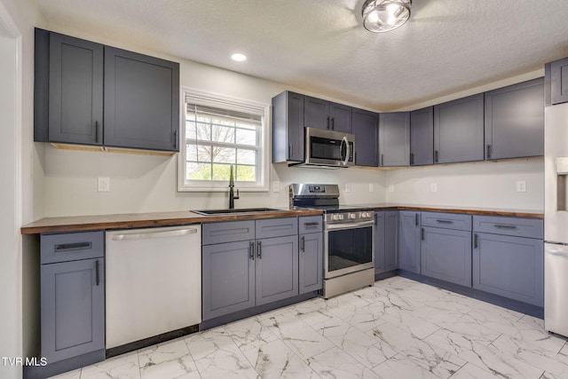 kitchen featuring stainless steel appliances, wood counters, light marble finish flooring, a sink, and recessed lighting