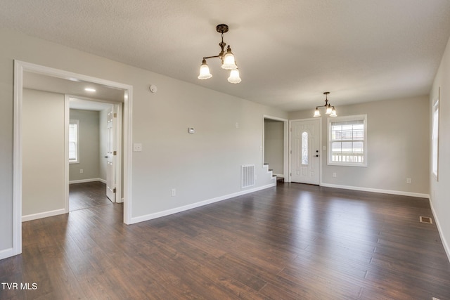 empty room with a chandelier, dark wood-style flooring, baseboards, and stairway