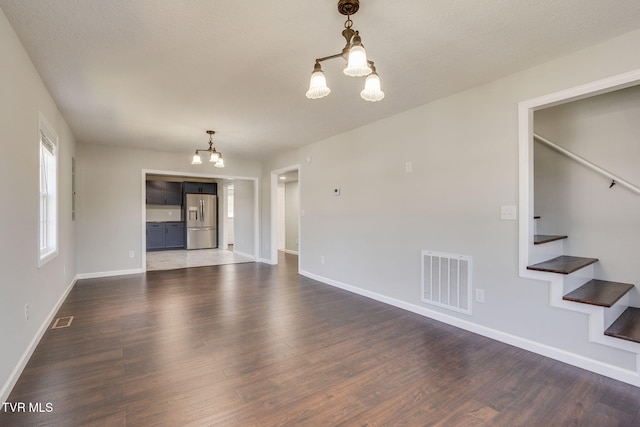 unfurnished living room featuring a chandelier, dark wood-style floors, baseboards, and stairs