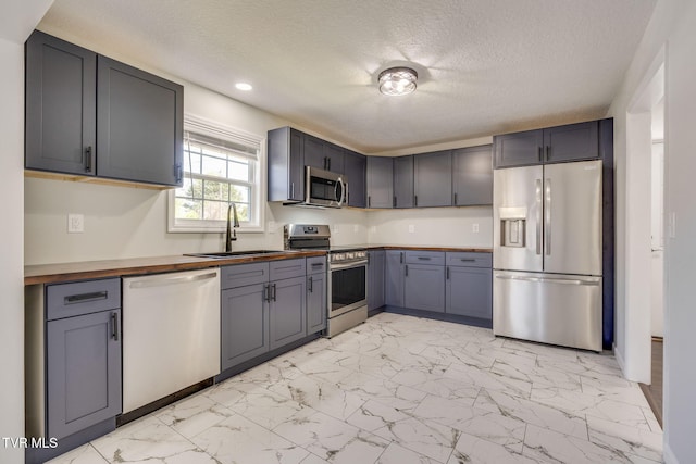 kitchen with stainless steel appliances, a sink, wood counters, light marble finish flooring, and recessed lighting