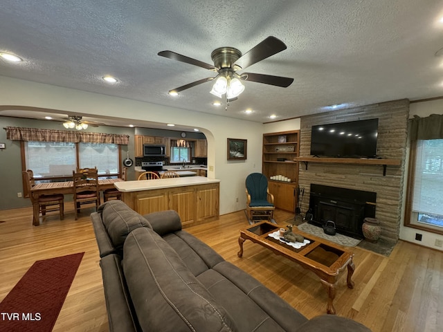 living area featuring arched walkways, a ceiling fan, a textured ceiling, and a fireplace