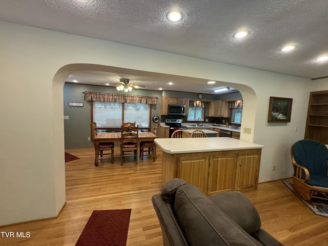 kitchen featuring stainless steel appliances, a ceiling fan, arched walkways, and light wood-style floors
