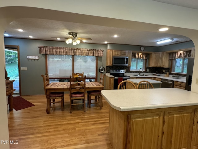 kitchen with arched walkways, light wood-style floors, stainless steel appliances, and a sink