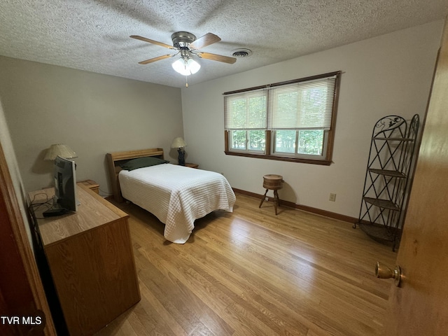 bedroom with light wood finished floors, a textured ceiling, baseboards, visible vents, and a ceiling fan
