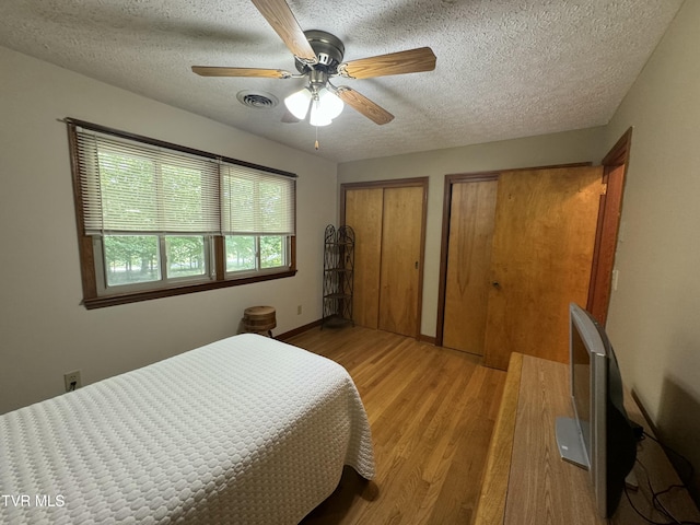 bedroom featuring a textured ceiling, multiple closets, ceiling fan, light wood-style flooring, and visible vents