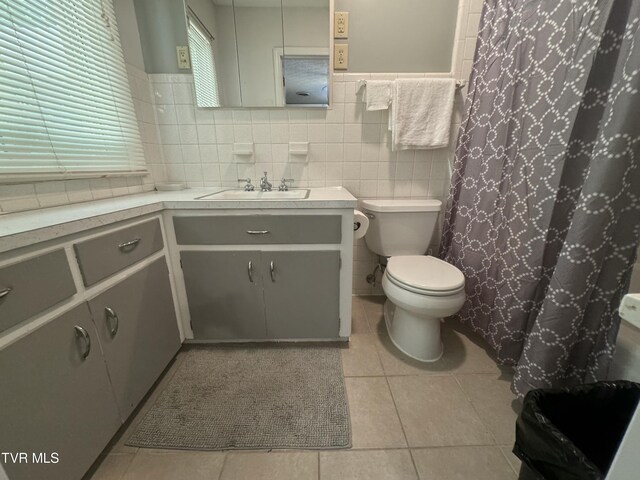 full bath with a wainscoted wall, tile patterned floors, toilet, vanity, and tile walls
