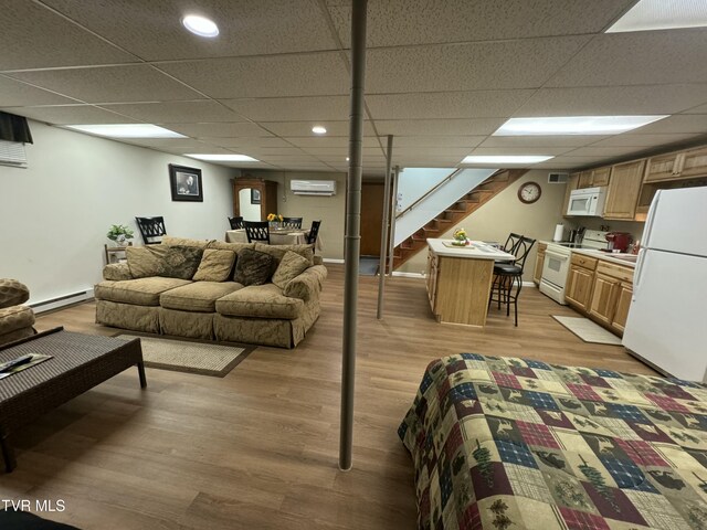 living room featuring light wood finished floors, a drop ceiling, a wall unit AC, baseboard heating, and stairs