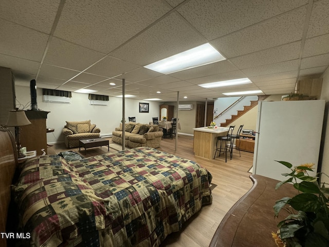 bedroom featuring a wall mounted air conditioner, freestanding refrigerator, light wood finished floors, and a paneled ceiling