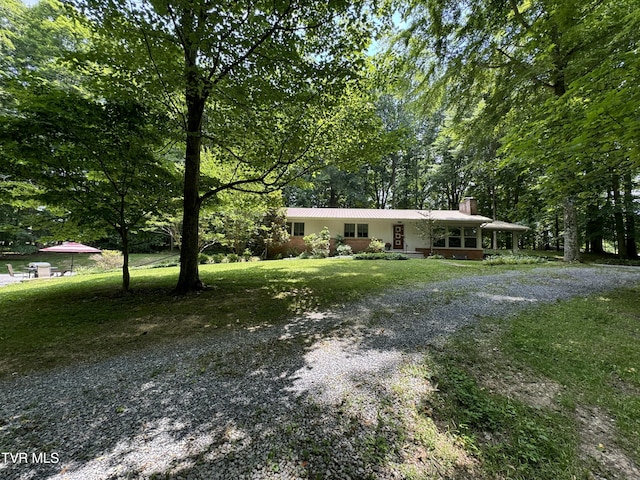 ranch-style house featuring driveway, a chimney, covered porch, and a front yard