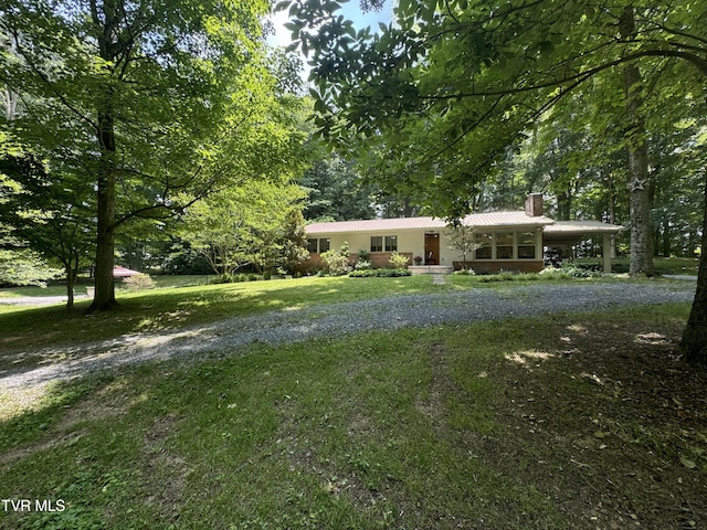 view of front facade featuring a chimney, a front lawn, an attached carport, metal roof, and gravel driveway