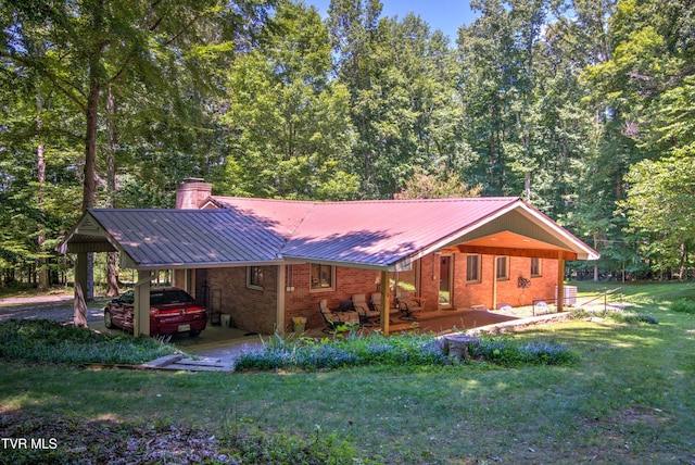 back of property featuring a chimney, a yard, an attached carport, brick siding, and metal roof