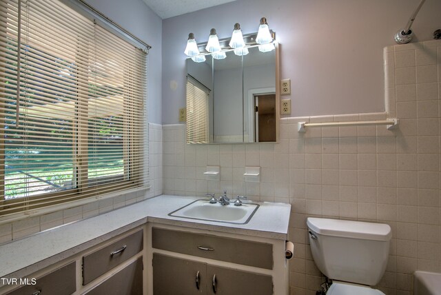 bathroom with tile walls, toilet, vanity, and wainscoting