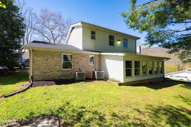 rear view of house featuring central AC, brick siding, and a lawn