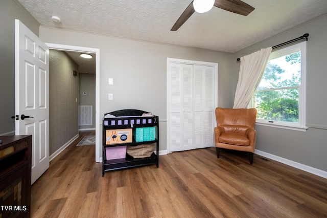 sitting room with wood finished floors, visible vents, baseboards, a textured ceiling, and ceiling fan