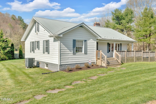 back of property with central AC, a chimney, a lawn, covered porch, and metal roof