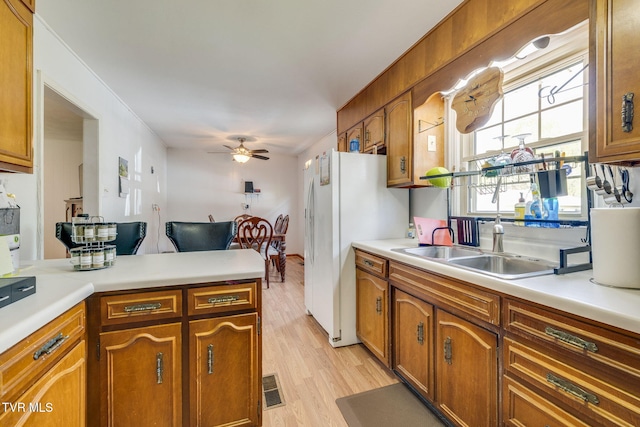 kitchen with brown cabinets, light wood-style floors, ceiling fan, light countertops, and freestanding refrigerator