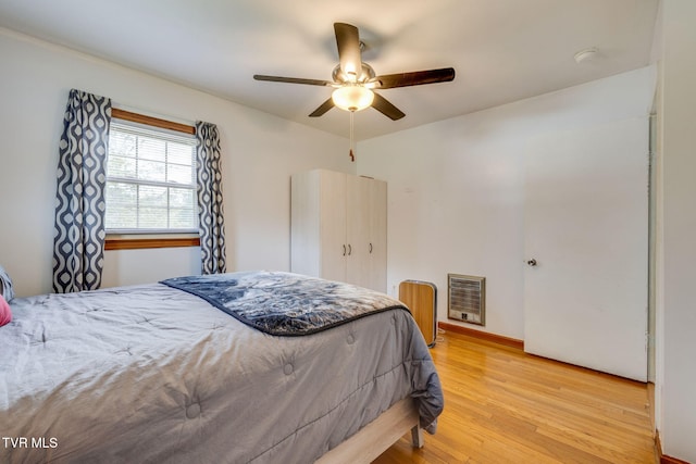 bedroom featuring light wood-style floors, a ceiling fan, and heating unit