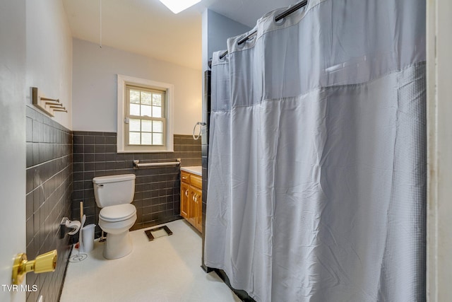 full bath featuring toilet, vanity, a shower with curtain, tile walls, and wainscoting