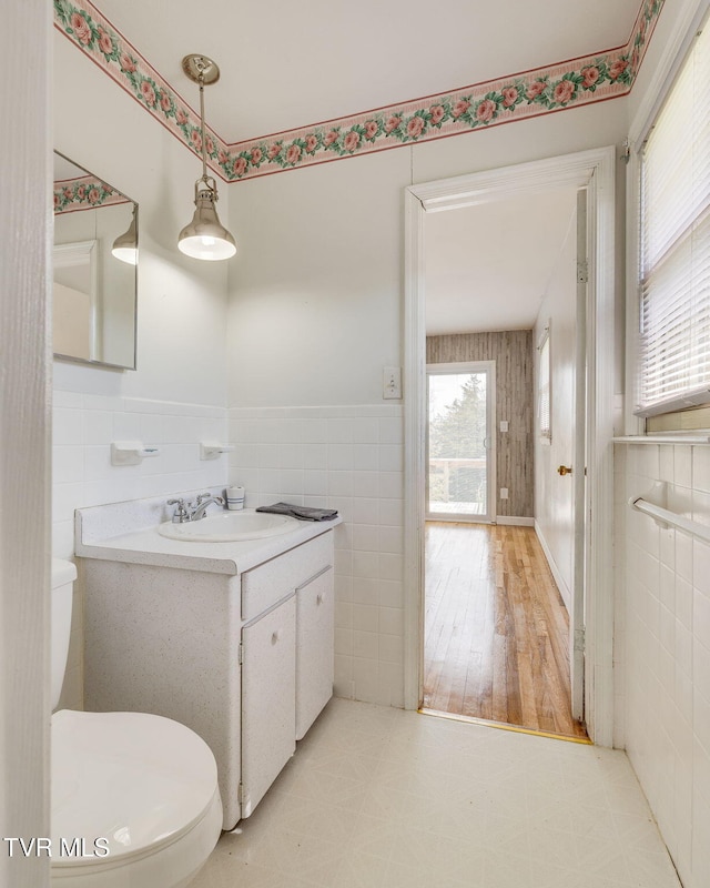 half bathroom featuring tile walls, a wainscoted wall, vanity, and toilet