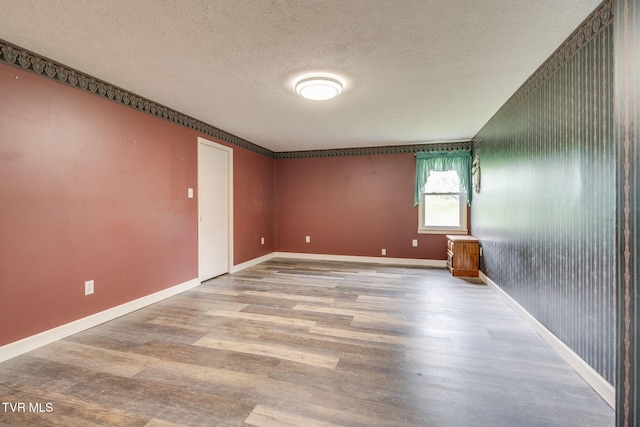 spare room with a textured ceiling, baseboards, and wood finished floors