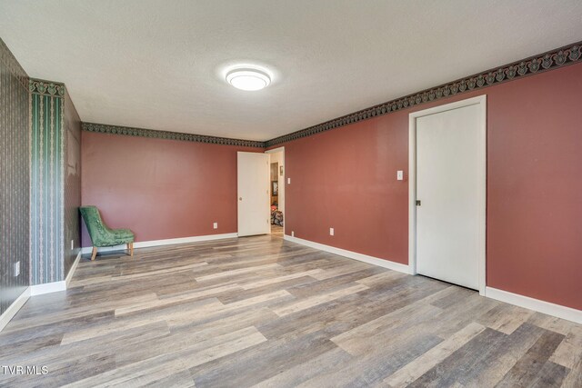 empty room with baseboards, a textured ceiling, and wood finished floors