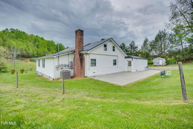 rear view of property featuring a patio, a lawn, a storage shed, and a chimney