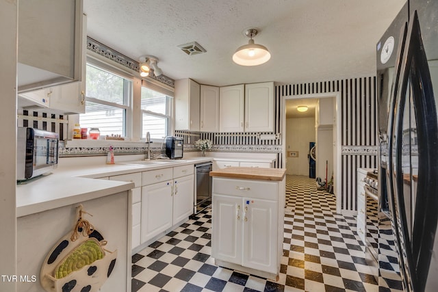 kitchen featuring visible vents, a sink, black appliances, light floors, and white cabinetry