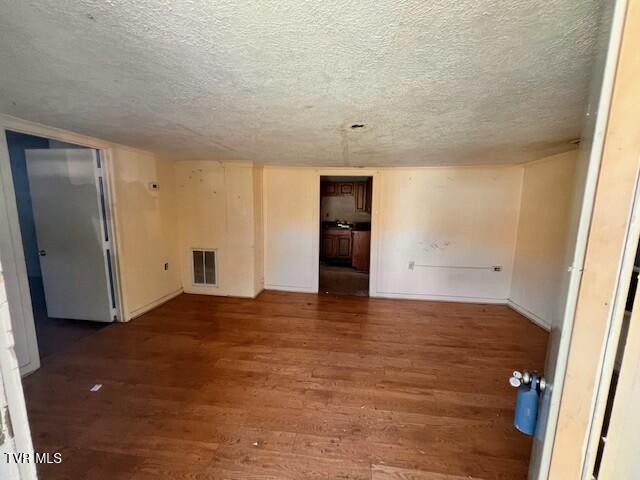 spare room featuring baseboards, wood finished floors, visible vents, and a textured ceiling