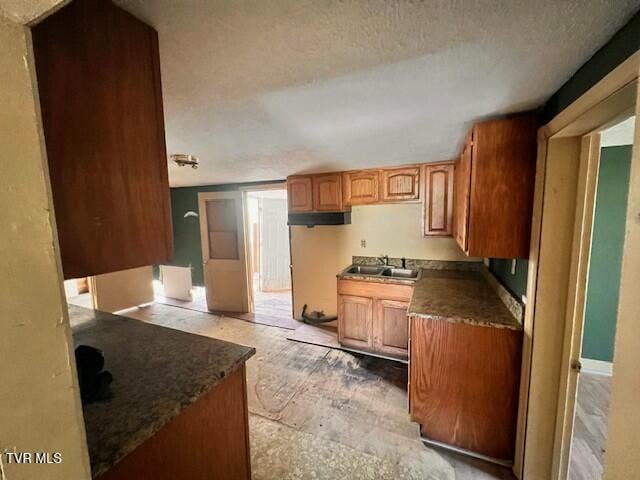 kitchen with dark countertops, a textured ceiling, a sink, and brown cabinets