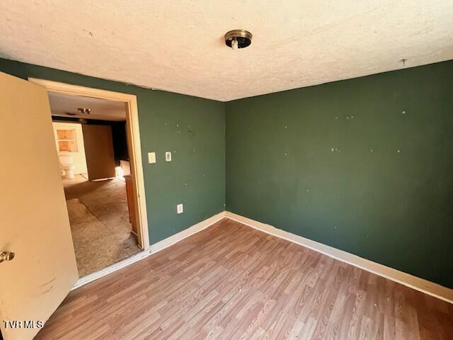 empty room with wood finished floors, a textured ceiling, and baseboards
