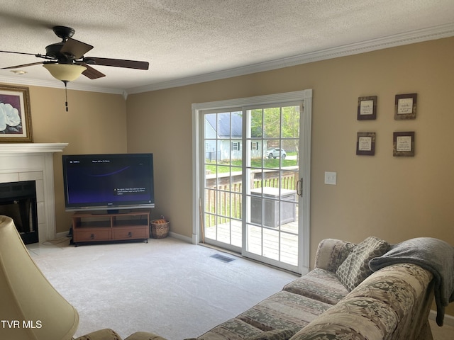 carpeted living room with crown molding, a textured ceiling, ceiling fan, a fireplace, and visible vents